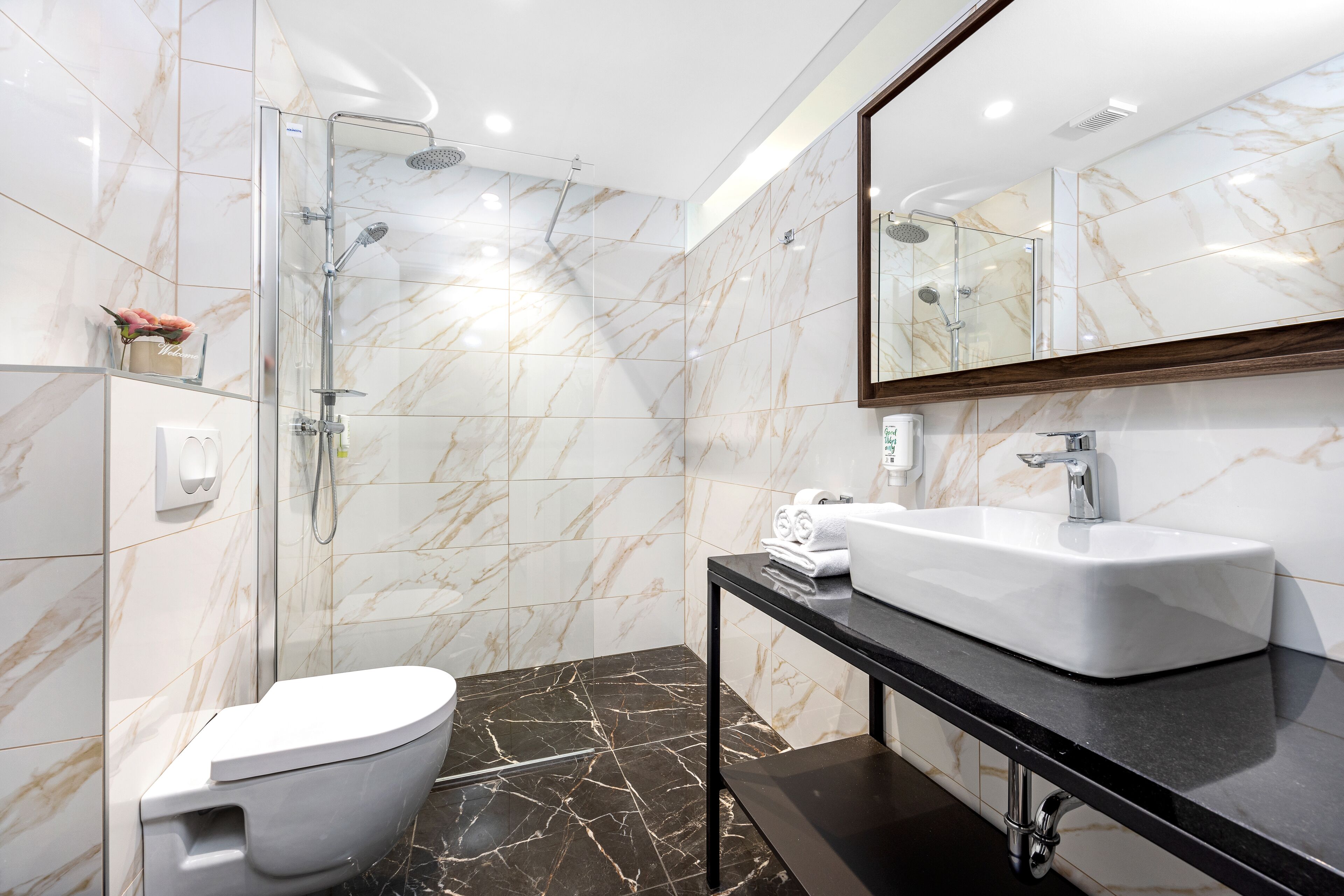 A modern bathroom with a glass-enclosed shower, a white sink, and a marble-tiled floor.
