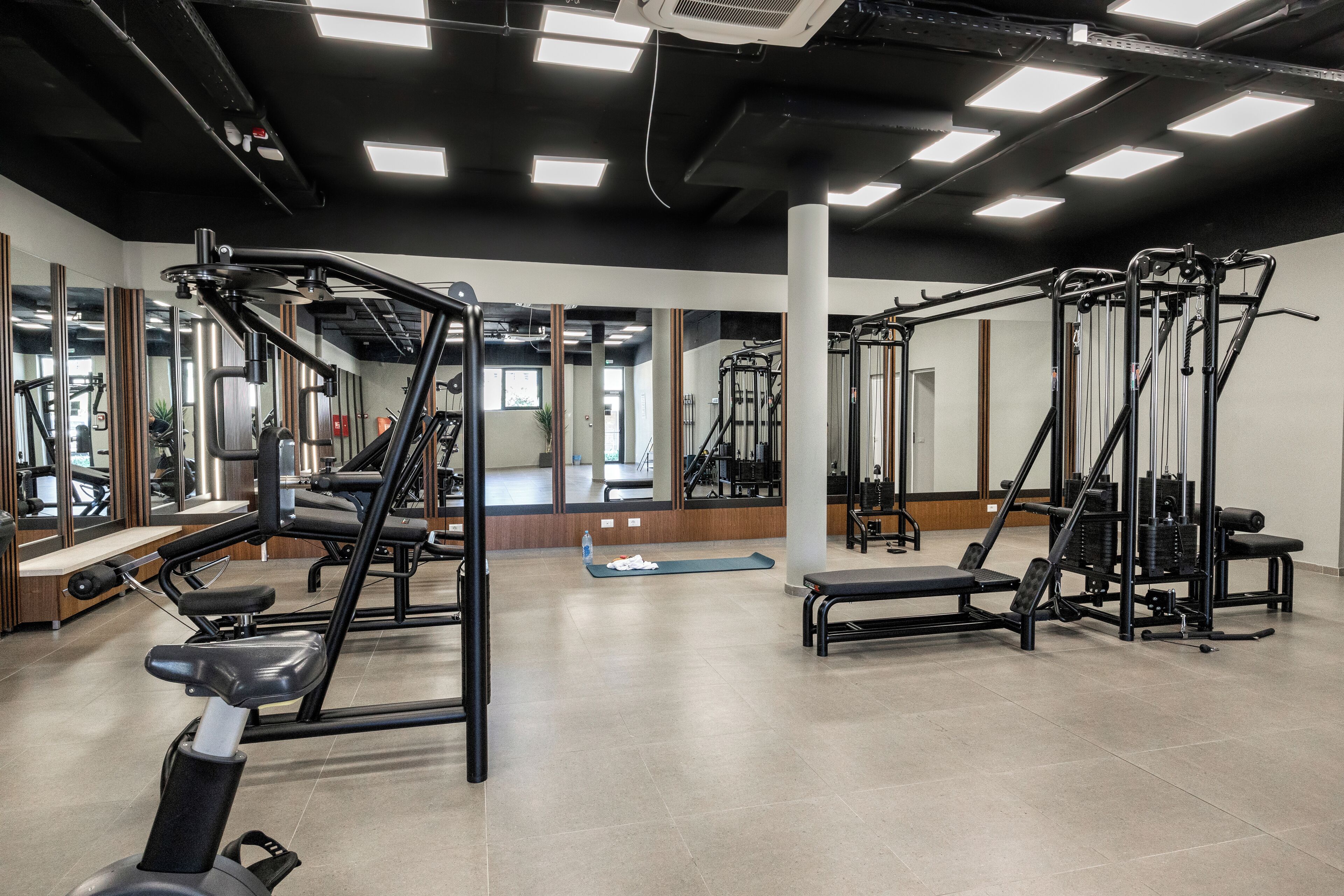A gym with various exercise equipment, mirrors, and a clean, tiled floor.