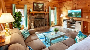 A cozy living room with a stone fireplace, a television, and a comfortable seating area. - A Smoky Mountain Lake Cabin, Spacious Smoky Mountain Getaway, Free Tickets! (Sevierville)