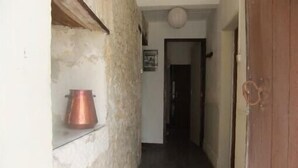 Un couloir étroit, avec un pot en cuivre posé sur une étagère, une porte sur la droite et un tableau encadré accroché au mur.