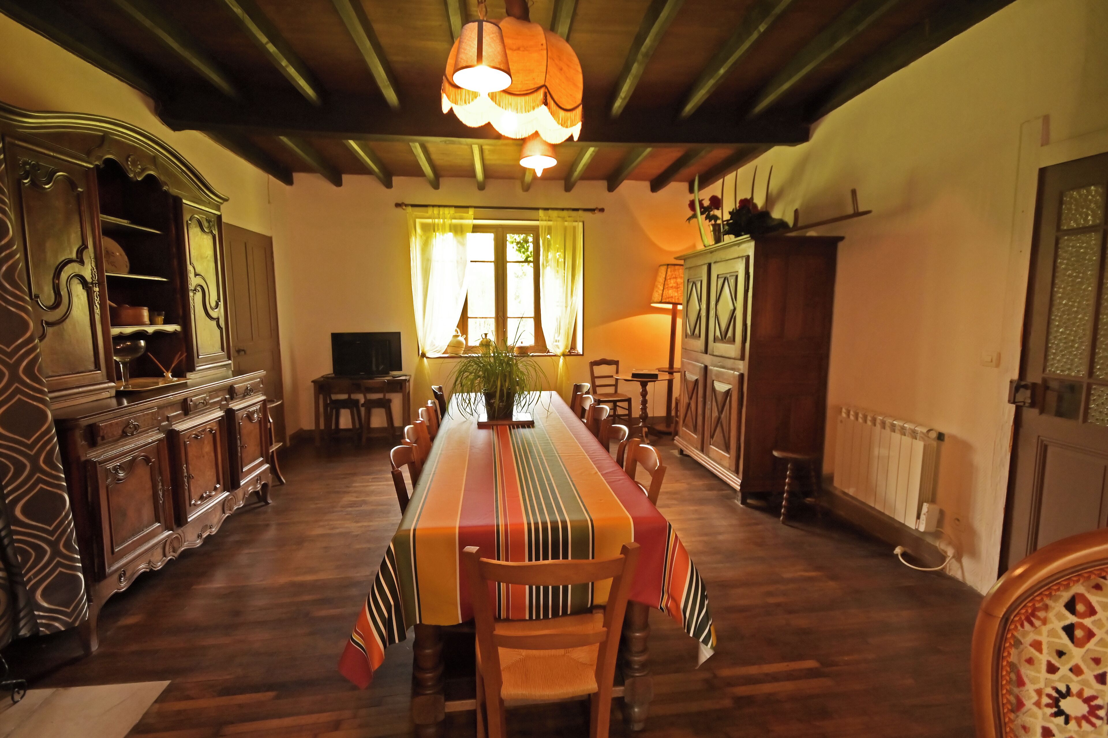 A dining room with a long wooden table, chairs, a chandelier, and a window with curtains.