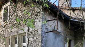 Un bâtiment rustique en pierre, doté d’un jardin comprenant un parterre surélevé et des plantes en pot.