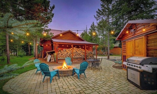 A wooden cabin with a fire pit, outdoor seating, and a grill area.