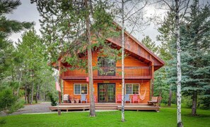 A two-story log cabin with a porch, surrounded by trees.