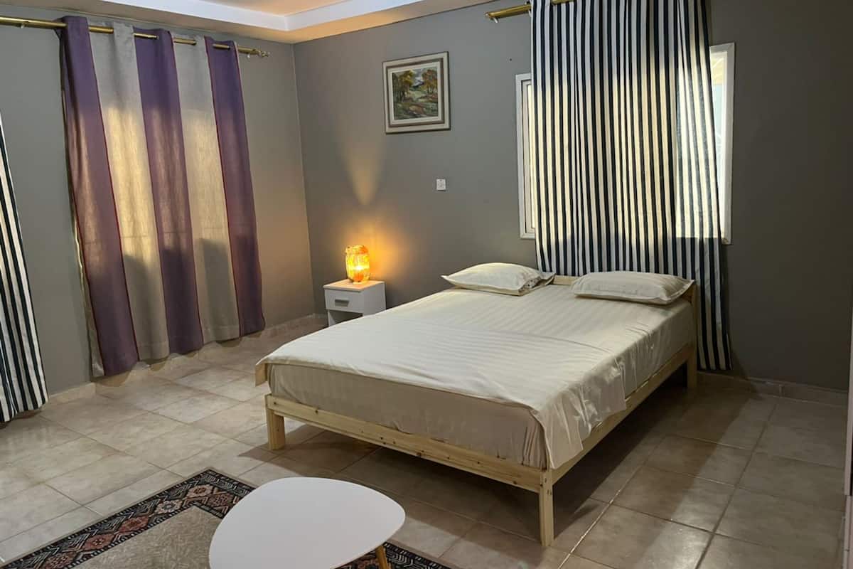 A bedroom with a bed, a bedside table with a lamp, curtains, and a rug.