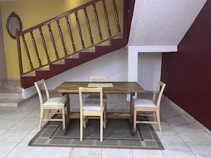 Ein Essbereich mit einem Holztisch, vier Stühlen, einem gemusterten Teppich und einer Treppe mit hölzernem Geländer.