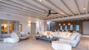A spacious living area with a high ceiling, a ceiling fan, and a stone wall. There is a white sofa, a round white chair, and a coffee table with decorative items.