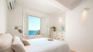 A bedroom with a large window, a bed, a dresser, and a mirror.
