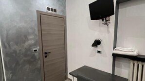 Une pièce moderne avec un mur gris, une porte en bois, un bureau avec une chaise, un téléviseur fixé au mur et un radiateur.