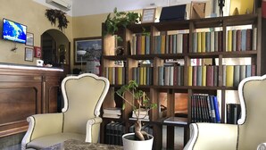 Une bibliothèque avec des étagères, deux chaises, une table, une plante en pot et un téléviseur fixé au mur.