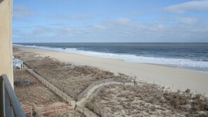 A beach view with a sandy shore, a wooden fence, and a clear sky.