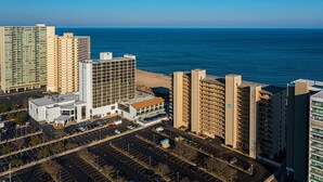 A high-rise hotel with multiple floors, a parking lot, and a view of the ocean.