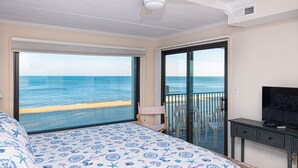 A bedroom with a large bed, a ceiling fan, a TV, and a view of the ocean.