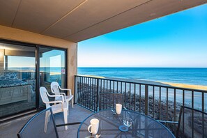 En balkon med udsigt over havet, et spisebord med stole og en seng med havudsigt.
