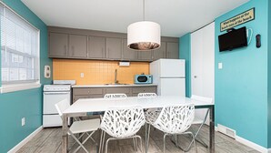 A kitchen with a white table, four white chairs, a microwave, a refrigerator, and a hanging light fixture. - Quaint, spacious 2 bedroom townhouse with free WiFi and an outdoor pool located downtown on the bayside and only three blocks to the beach! (Ocean City)
