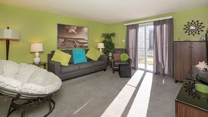 A living room with a sofa, armchair, and a large window with curtains. - Quaint, spacious 2 bedroom townhouse with free WiFi and an outdoor pool located downtown on the bayside and only three blocks to the beach! (Ocean City)
