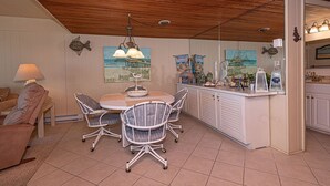 A kitchen with a round table, four chairs, a wooden ceiling, and various kitchen appliances.