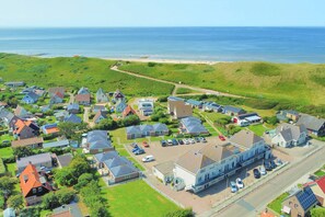 A coastal residential area with houses, a parking lot, and a beach in the background.