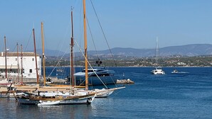 Ein Yachthafen mit verschiedenen Schiffen, darunter Segelboote und Yachten, vor einer Hügelkulisse und bewölktem Himmel.