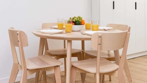 Ein Essbereich mit einem runden Tisch, vier Stühlen, einer Obstschale und Gläsern Orangensaft.