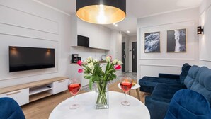 Un salon moderne avec un téléviseur à écran plat, une table basse ronde sur laquelle reposent deux verres à vin, un vase rempli de fleurs et un canapé bleu.