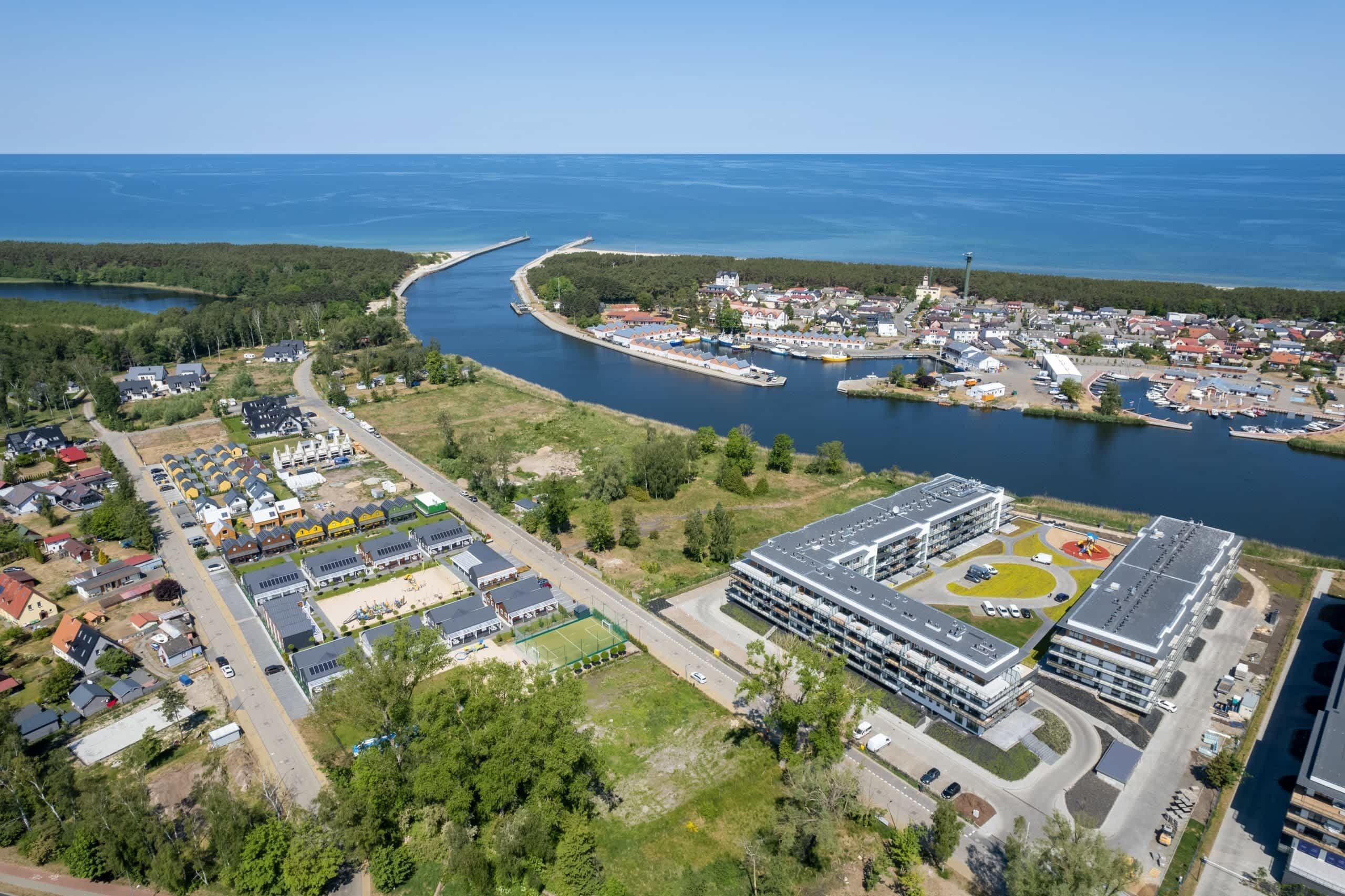 Vista aèria d'una població costanera amb zones residencials, un port esportiu i un edifici gran amb un camp esportiu.