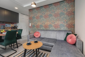 A modern living space with a grey sofa, a small round table, and a vibrant patterned wall. - Stylish Apartment | Terrace and Jacuzzi in the Building (Międzywodzie)