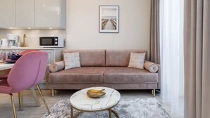 Ein modernes Wohnzimmer mit einer Couch, einem rosa Sessel, einem Couchtisch und einer Küchenzeile im Hintergrund.
