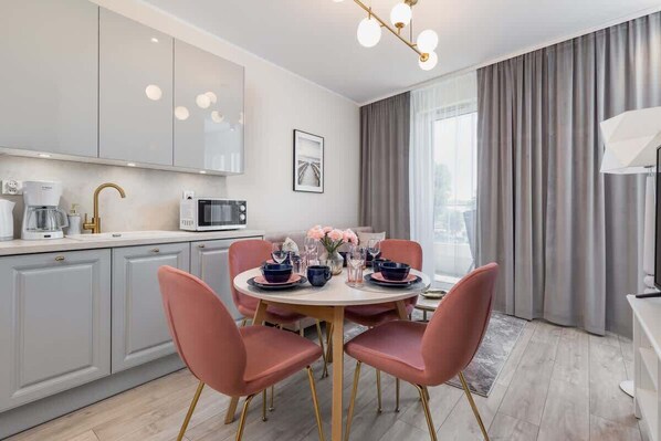 A modern kitchen with a dining area, including a round table with pink chairs, a coffee machine, and a microwave.