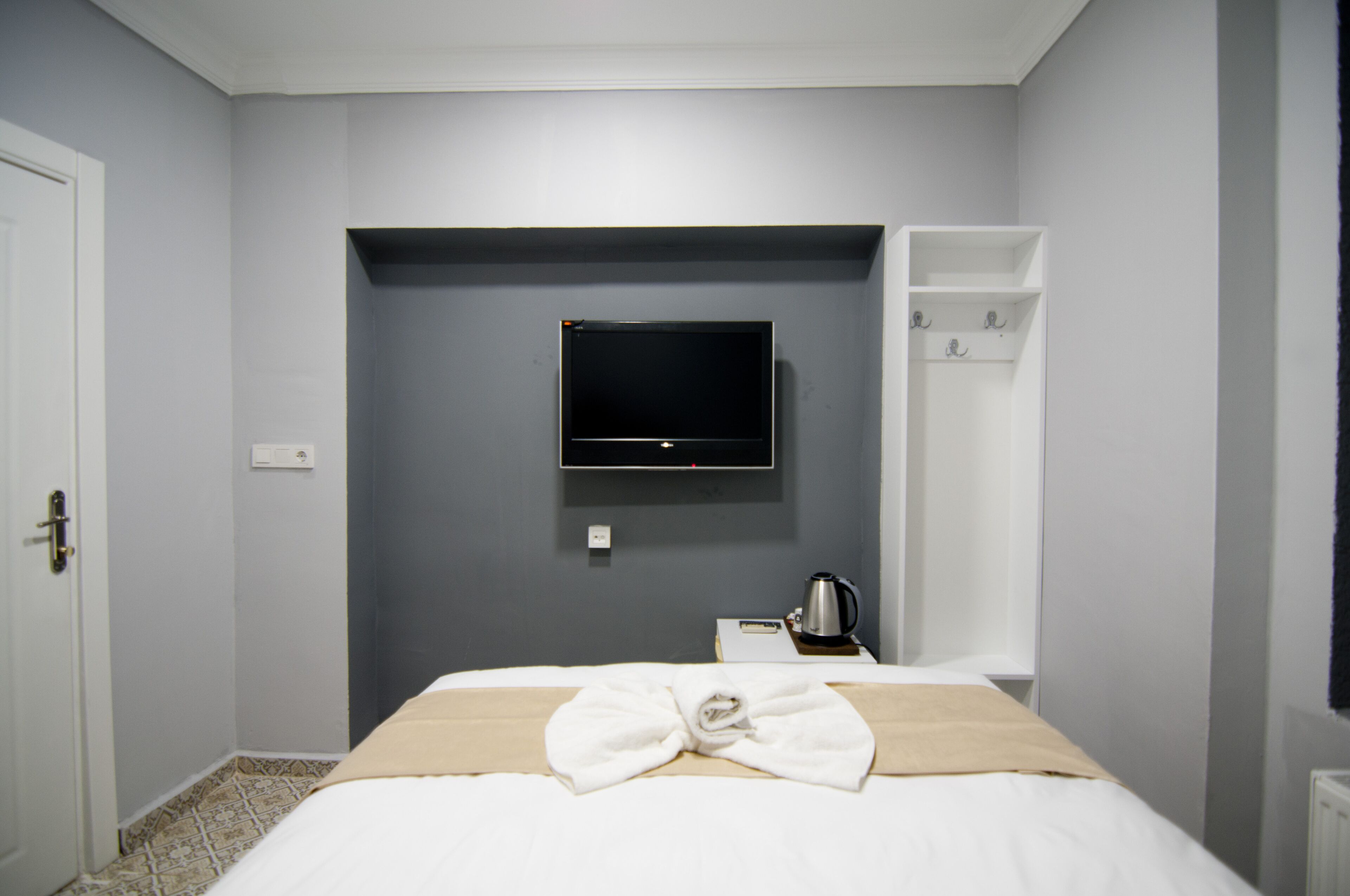 Quarto de hotel com cama, televisão na parede, cafeteira e um porta-casacos.