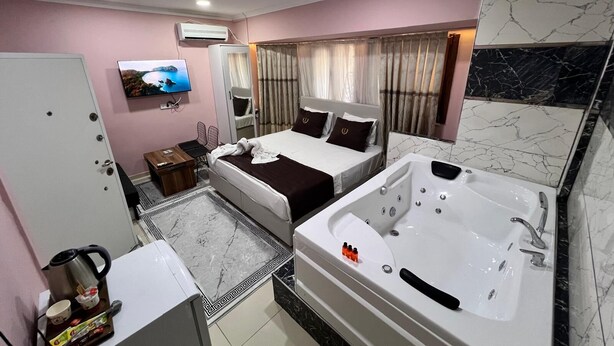 Habitación de hotel con cama, zona de estar con televisor, baño con bañera y cafetera.