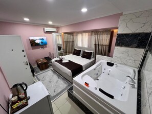 Une chambre d’hôtel comprenant un lit, un coin salon avec un téléviseur, une salle de bain avec une baignoire et une machine à café.