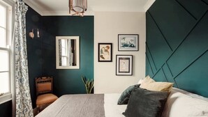 A bedroom with a bed, a chair, a mirror, and framed pictures on the wall.