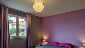 Ein Schlafzimmer mit Bett, Vorhängen, einem Fenster, einer Lampe und einer Wandleuchte.