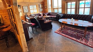 A wooden interior with a large leather sofa, a round table, and a view through large windows. - Sirevåg Hotel (Ha)