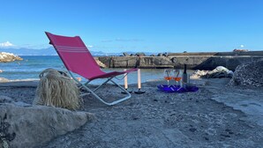 Ein Strand mit einem rosafarbenen Liegestuhl, einem Korbwannen und einem Tablett mit Gläsern und einer Flasche.