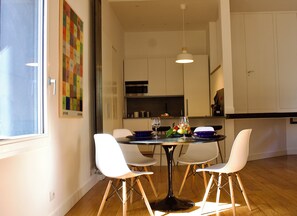 A modern dining area with a round table, four white chairs, and a hanging light fixture.