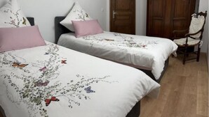 Zwei Einzelbetten mit blumigem und schmetterlingsmusterbezogenem Bettzeug, ein Holzschrank und ein Holzstuhl in einem Zimmer mit Holzboden.