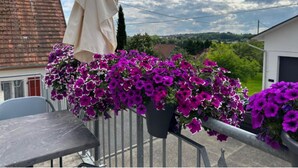 Ein Balkon mit Metallgeländer, Tisch und hängenden violetten Blüten.