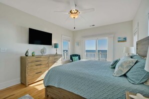 A bedroom with a bed, a dresser, a television, and a balcony with a view.
