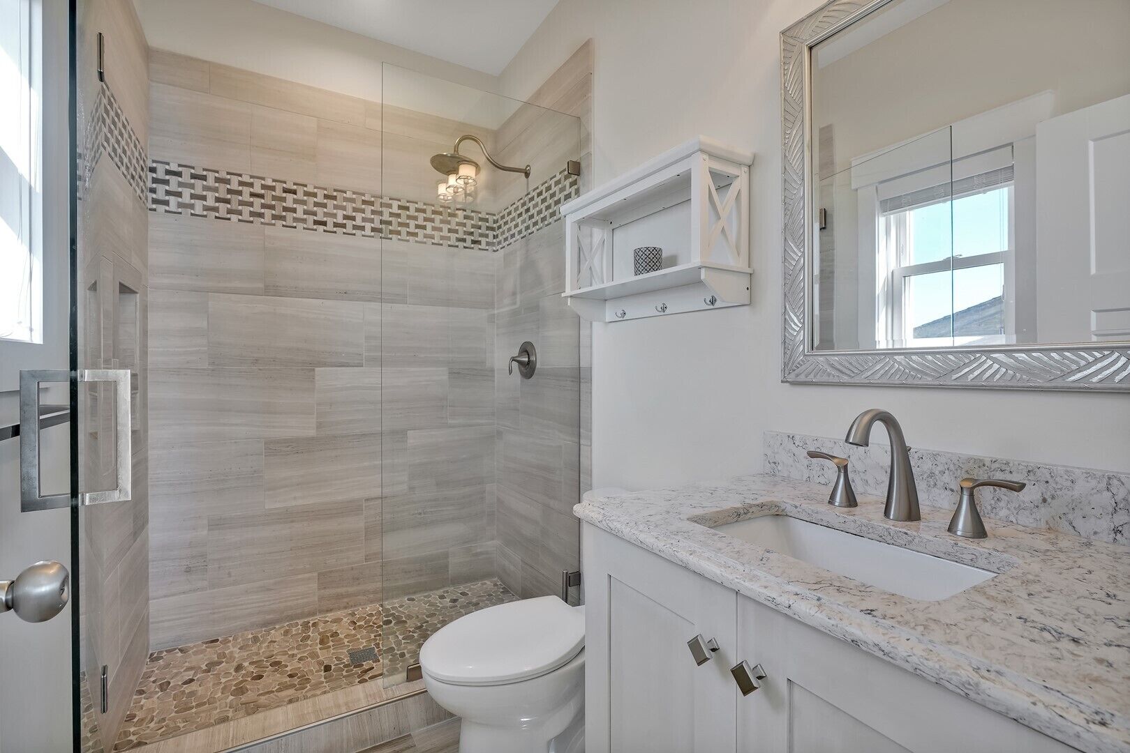 Een moderne badkamer met een glazen douchecabine, een wit toilet en een marmeren aanrecht met een wastafel en twee kraanwerk.