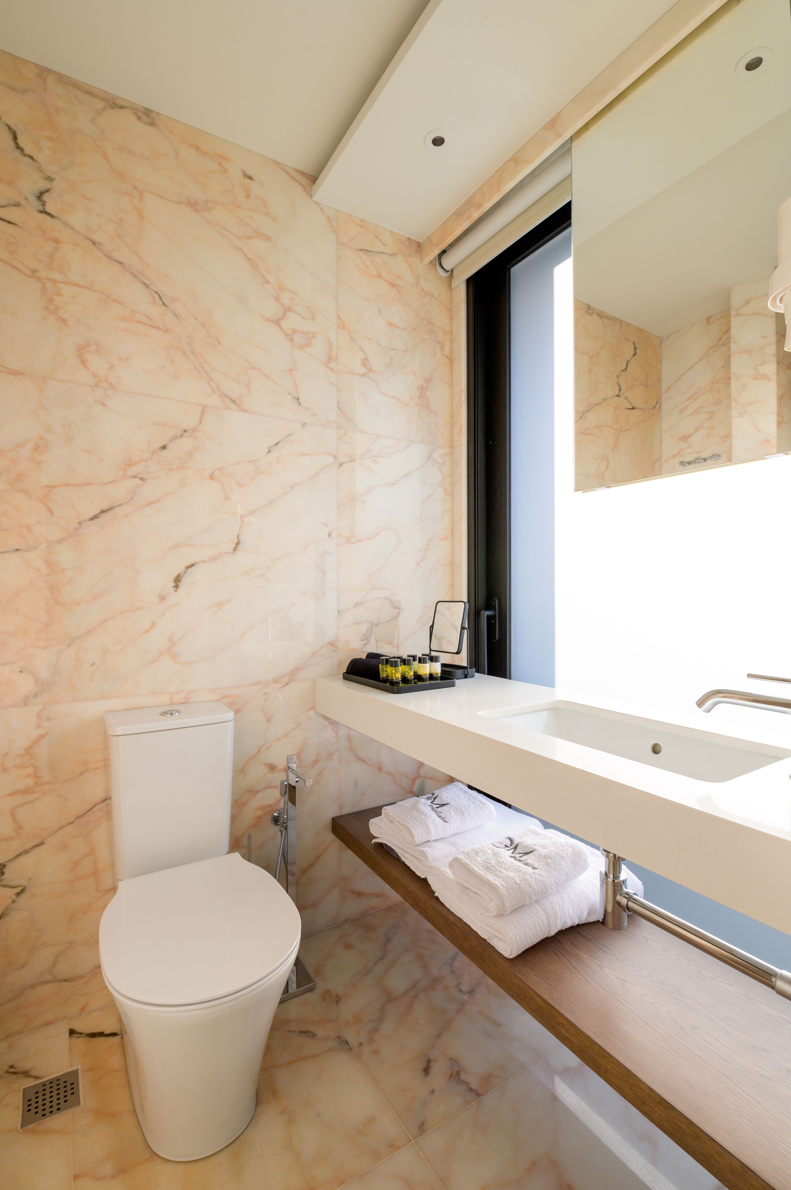 A modern bathroom with a marble wall, a toilet, a sink with a mirror, and a towel rack.