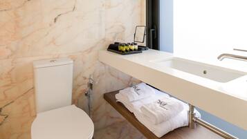 A modern bathroom with a marble wall, a toilet, a sink with a mirror, and a towel rack.