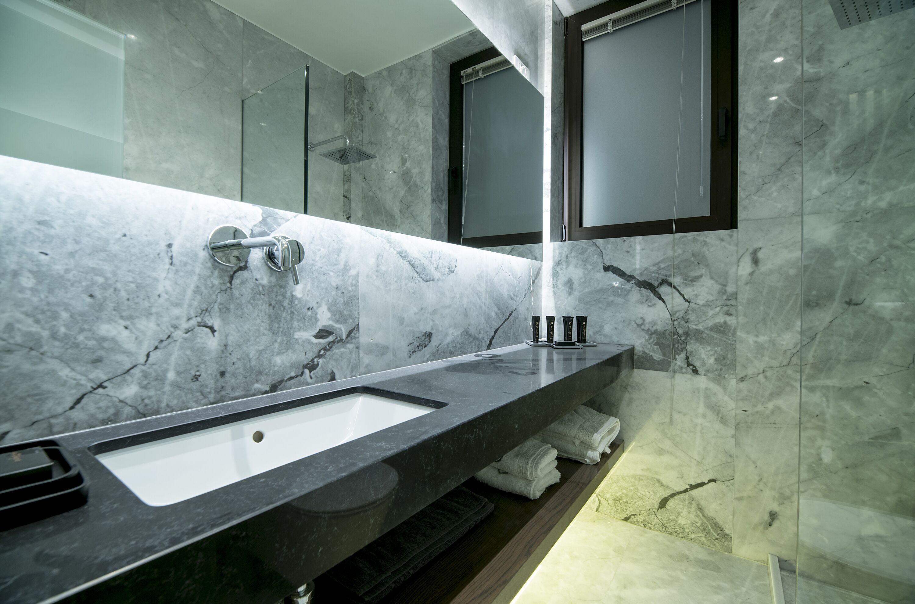 A modern bathroom with a marble sink, a glass shower enclosure, and neatly folded towels on a shelf.