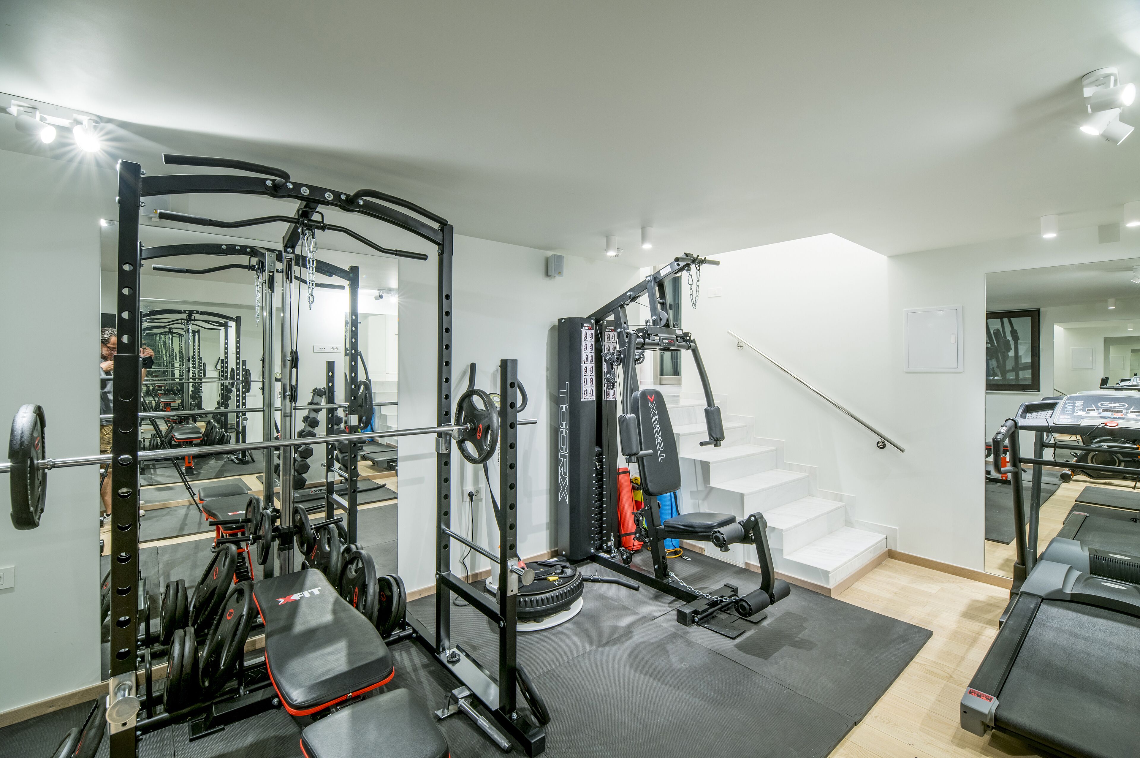 A home gym with a squat rack, bench press, and treadmill.