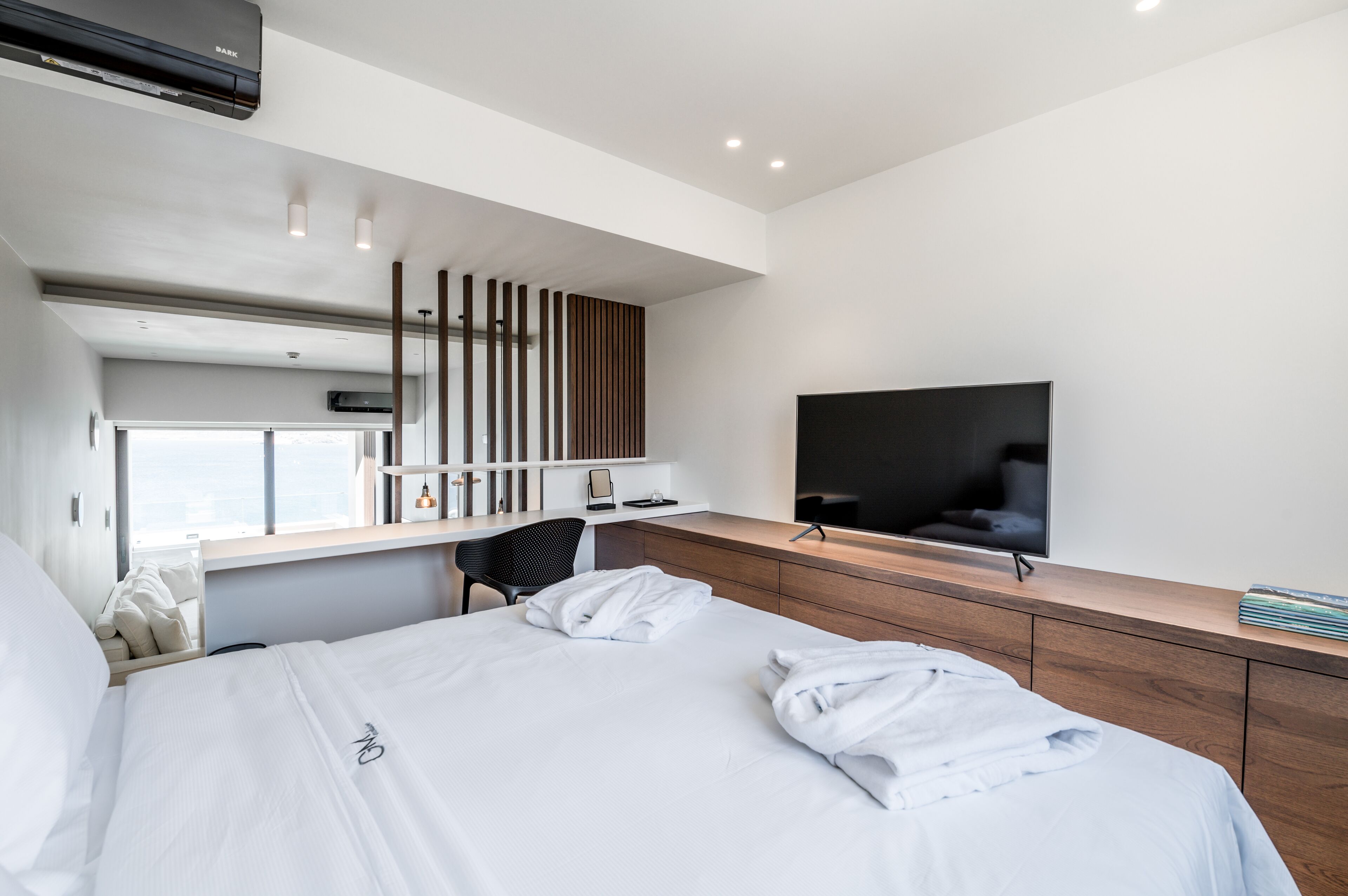A modern hotel room with a large bed, a desk with a chair, a flat-screen TV, and a large window.