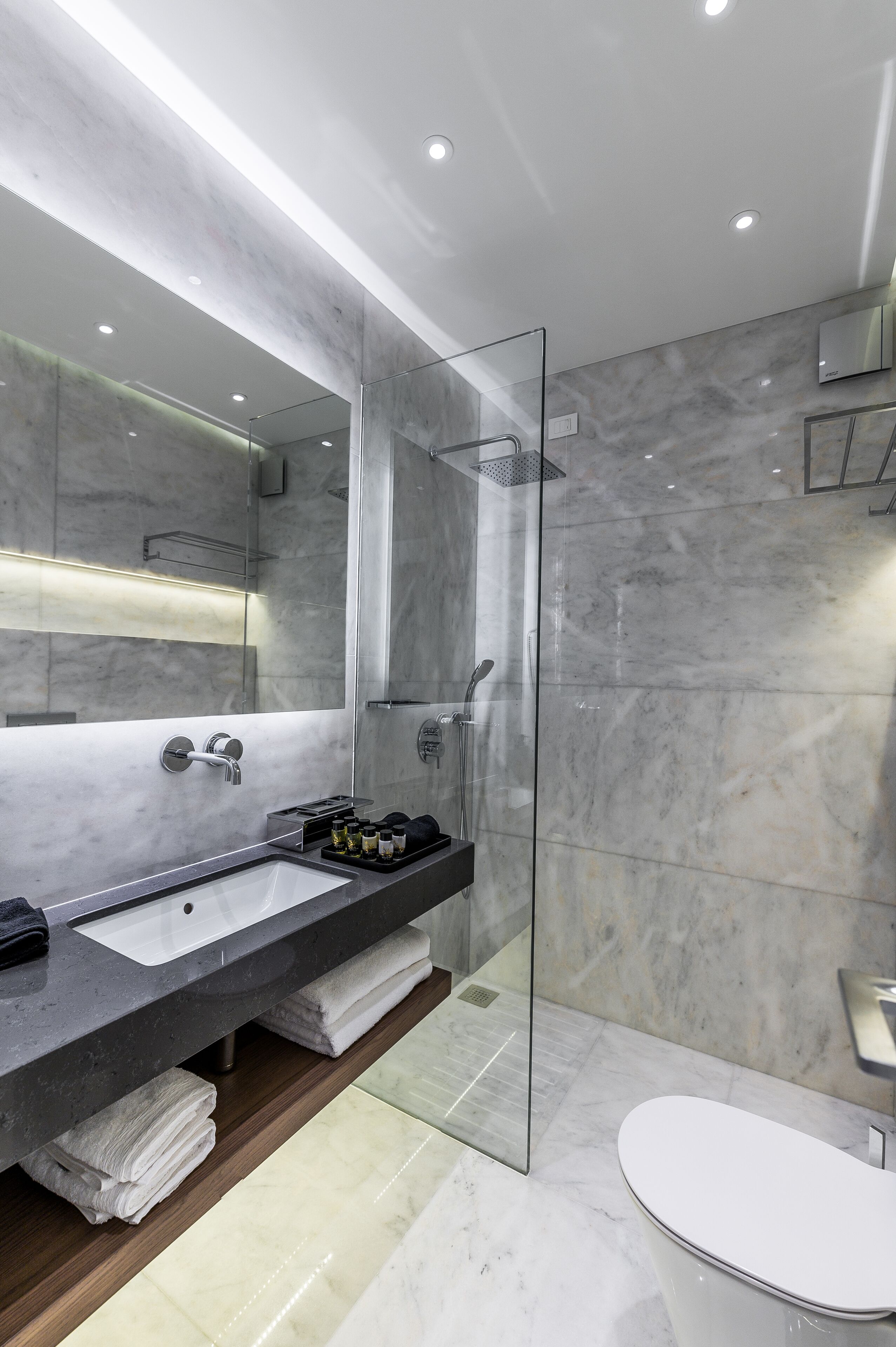 A modern bathroom with a marble sink, a glass shower enclosure, and a white toilet.