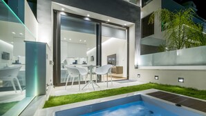 A modern outdoor pool area with a glass-enclosed patio and a dining set. - GM Luxury Suites & Spa (Sitia)