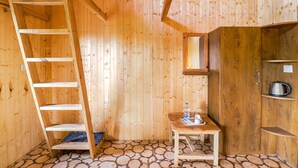 Ein Holzblockhaus-Innenraum mit einer Holzleiter, einem kleinen Tisch mit einer Wasserflasche und einem Wasserkocher auf einem Regal.