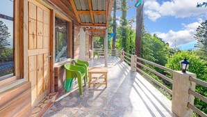 Ein Holzbalkon mit Fliesenboden, grünen Stühlen und einem Tisch.